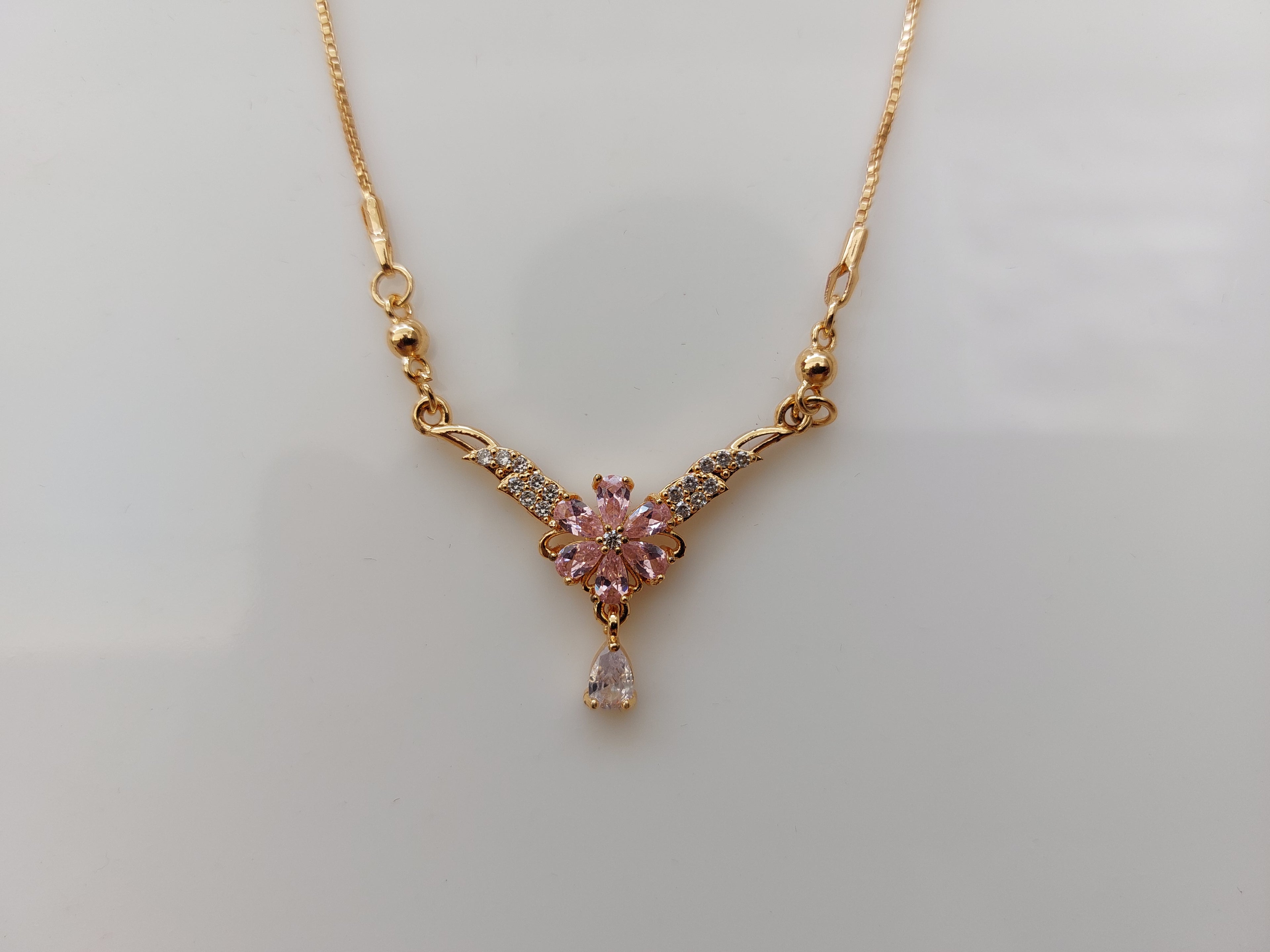 A gold Y-shaped necklace with a central pink flower pendant and small clear accent stones, displayed on a plain light background.