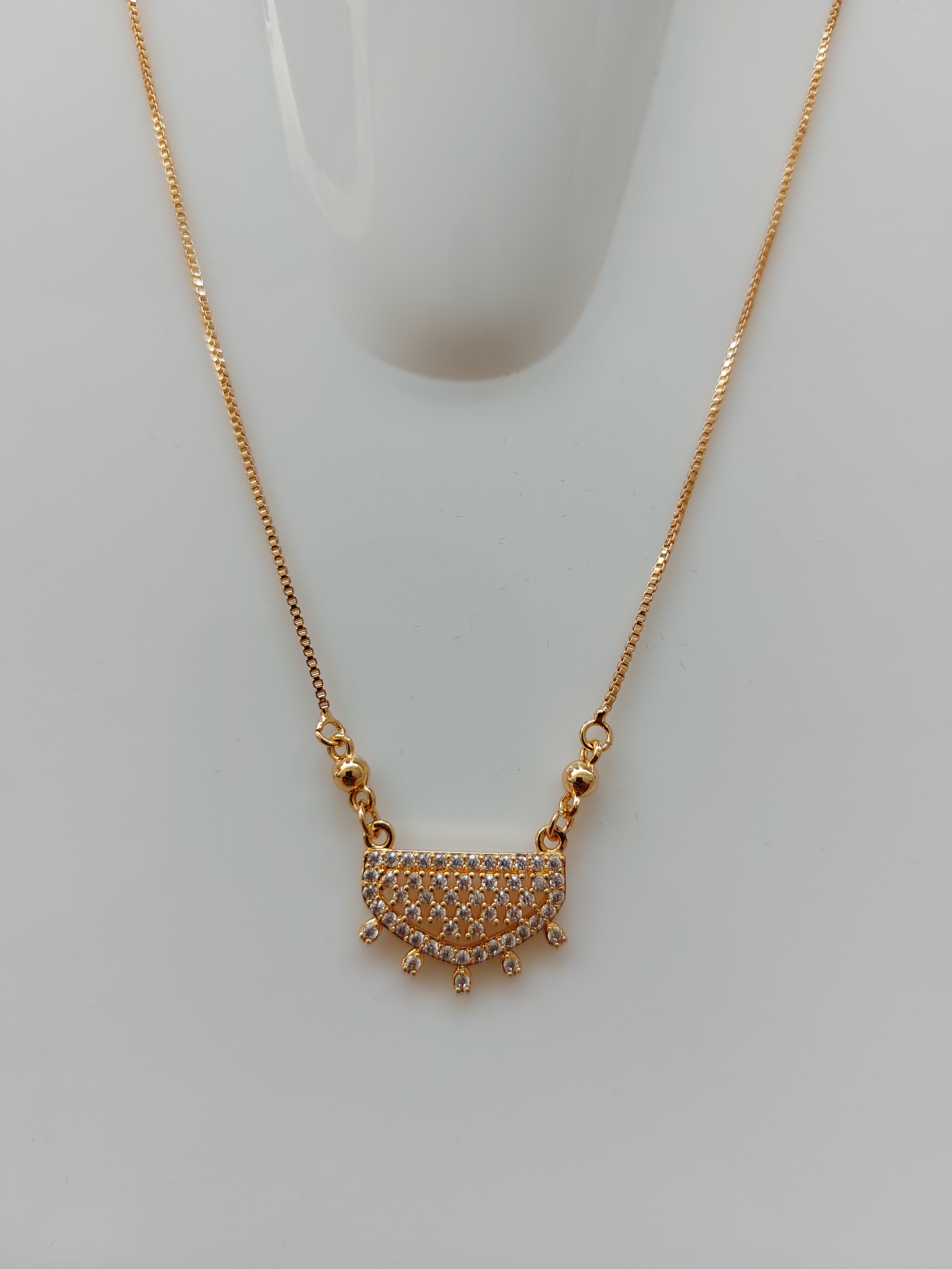 A gold chain necklace with a semi-circular pendant paved with small clear stones and featuring small gold spikes along the curved top edge, displayed on a white mannequin bust against a light gray background.
