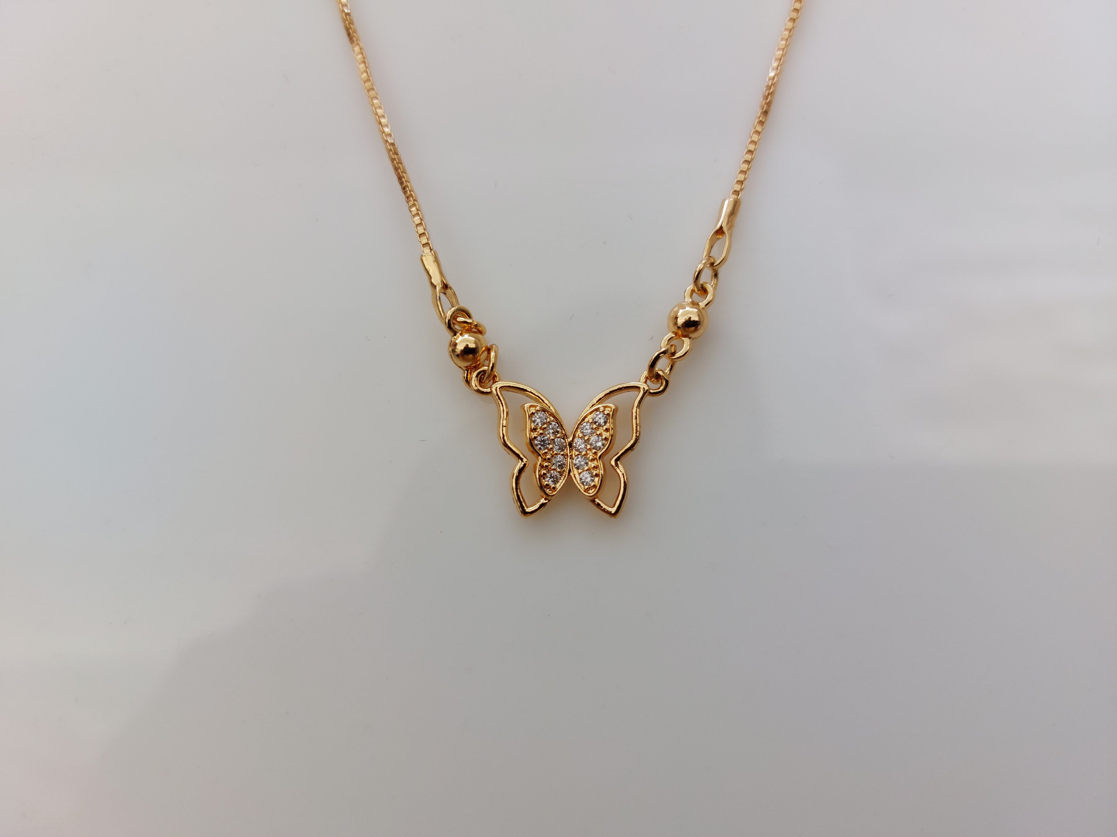 A gold butterfly pendant necklace with a small cluster of clear stones in the center, displayed on a plain light gray background.
