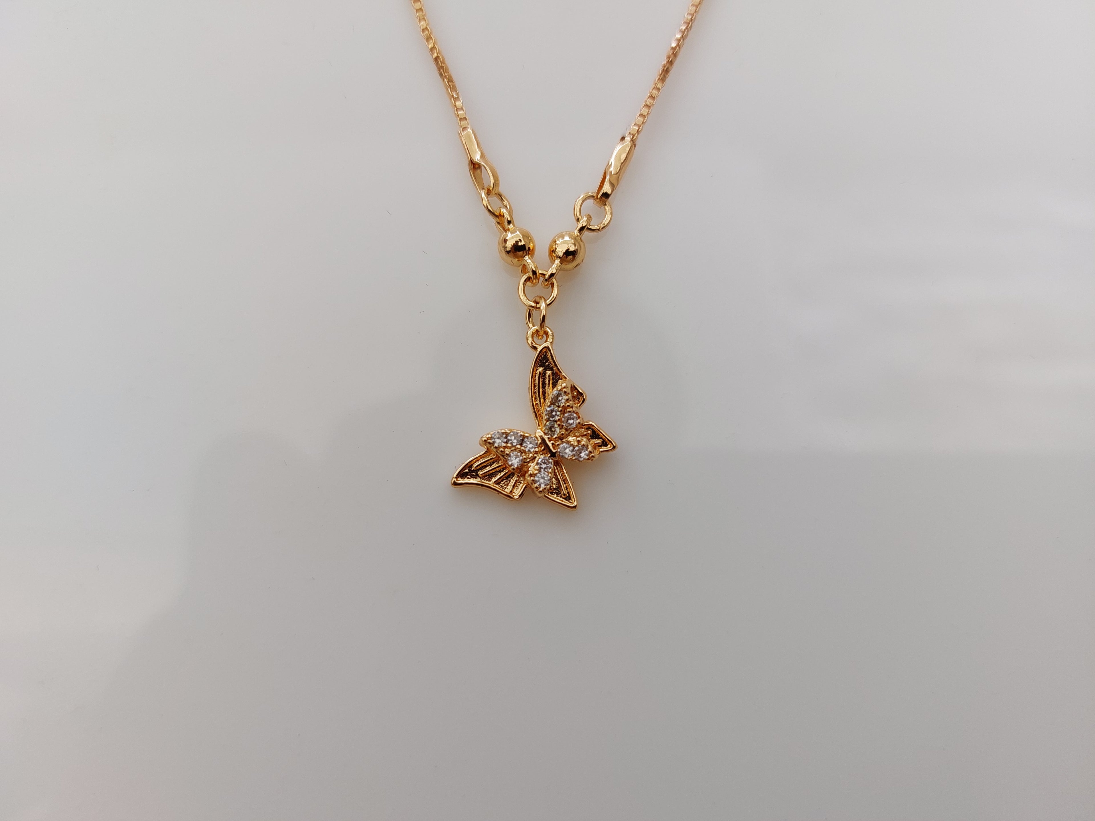 A gold butterfly pendant necklace with small clear rhinestones on its wings, shown on a plain light gray background.