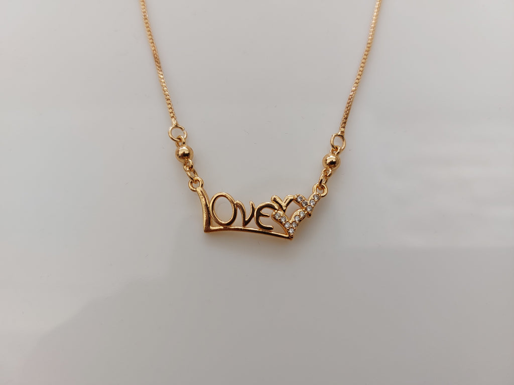 A gold chain necklace featuring a 'LOVE' pendant with a small heart made of clear stones, displayed on a plain light gray background.