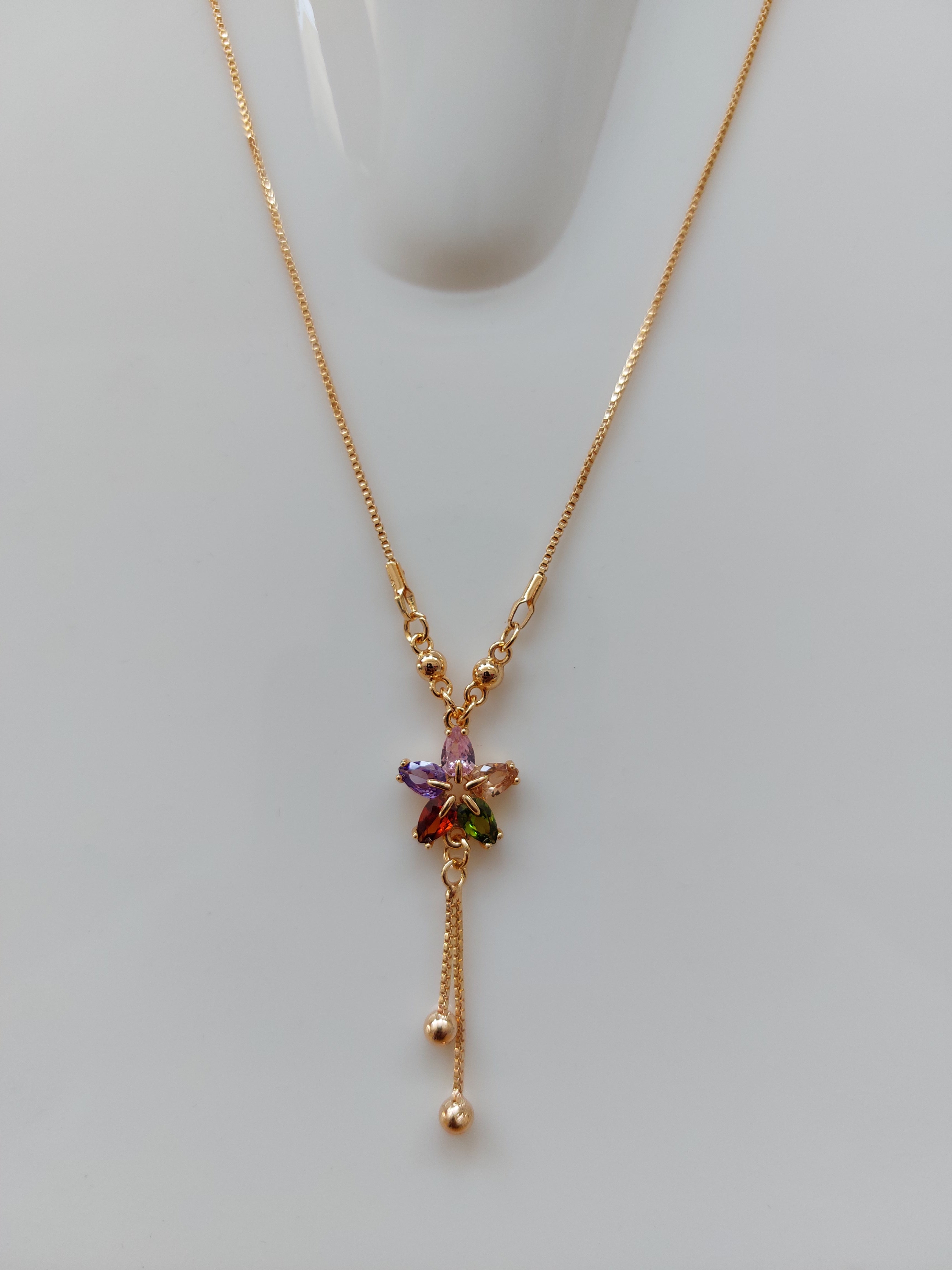 A delicate gold chain necklace with a central floral cluster of small multicolored gemstones, displayed on a light gray surface.