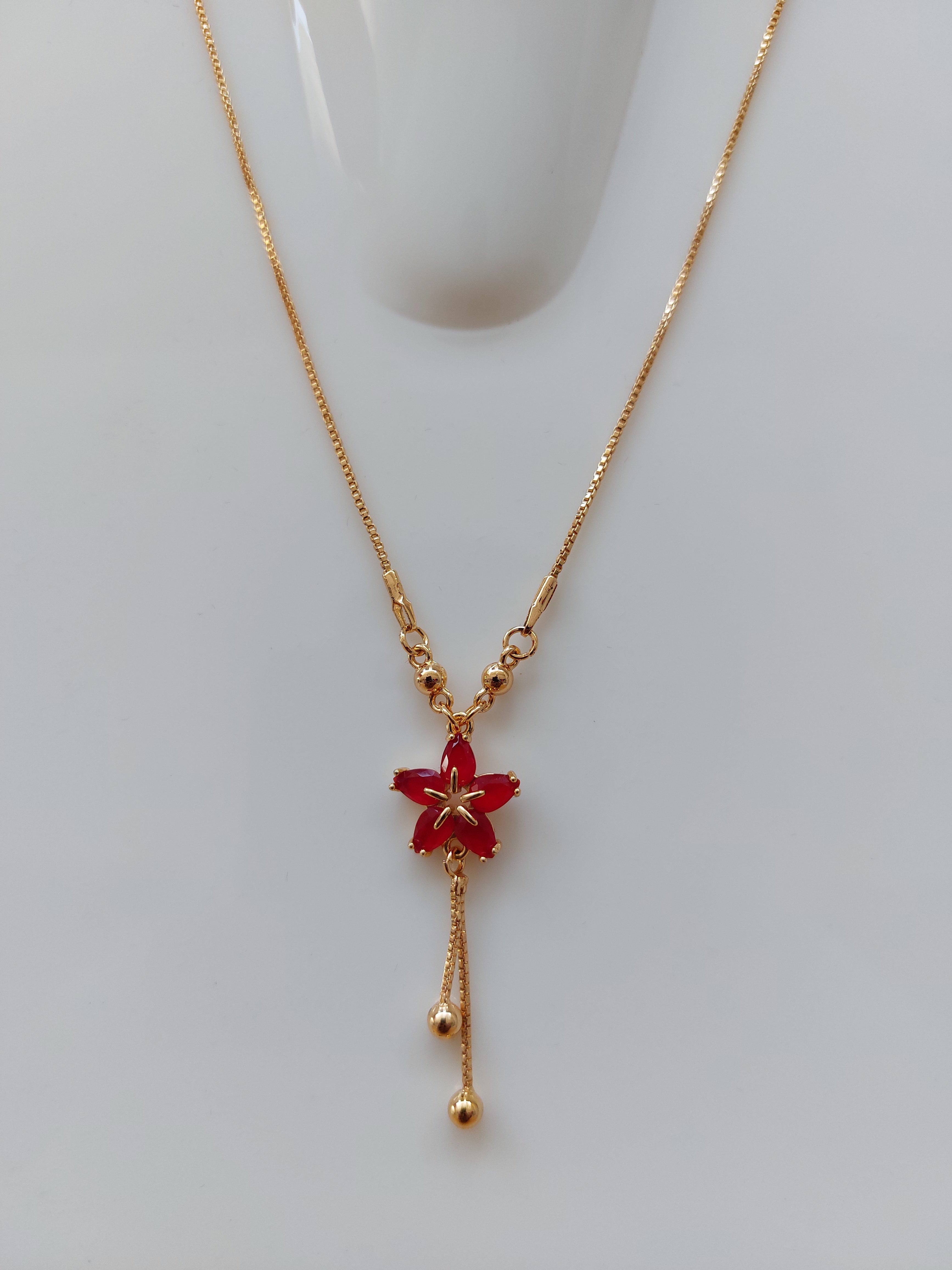 A delicate gold Y-shaped necklace featuring a small red flower pendant, displayed on a light gray surface.