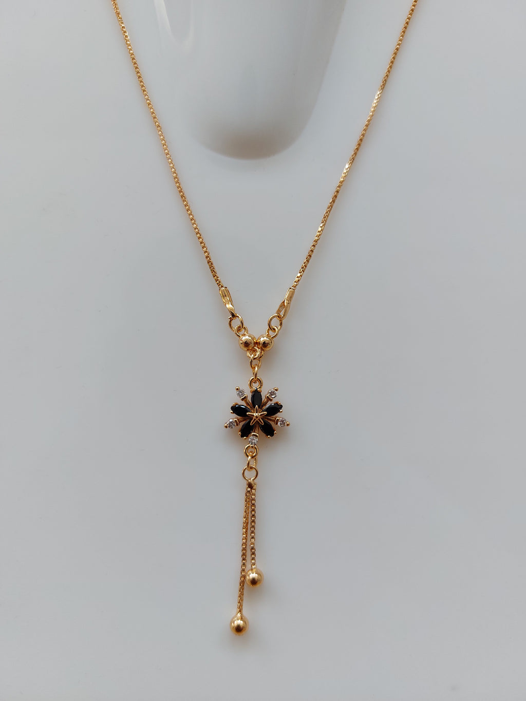 A delicate gold chain necklace with a Y-shaped design, featuring a central black floral starburst charm and two dangling chain ends, displayed on a light gray surface.