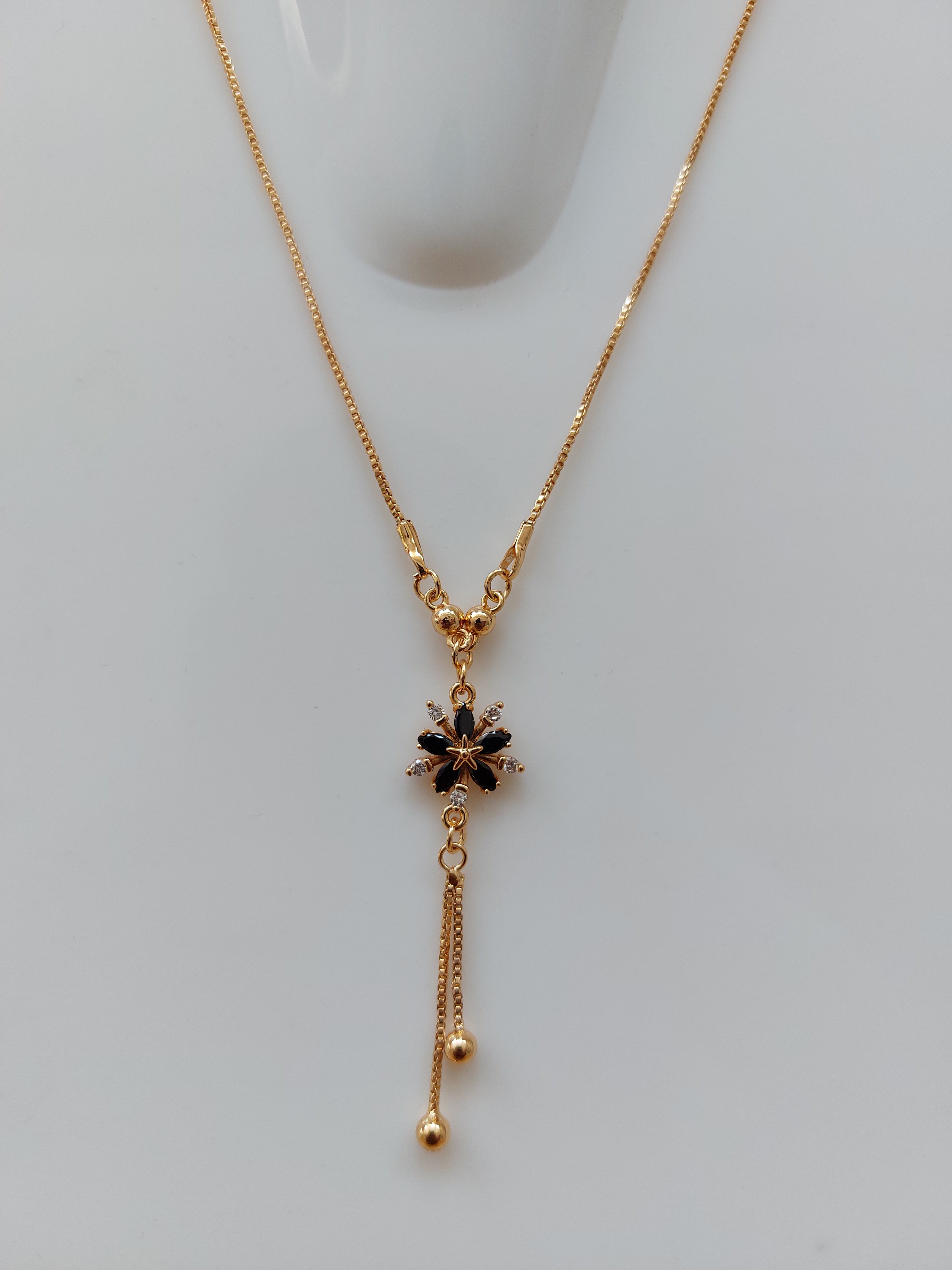 A delicate gold chain necklace with a Y-shaped design, featuring a central black floral starburst charm and two dangling chain ends, displayed on a light gray surface.