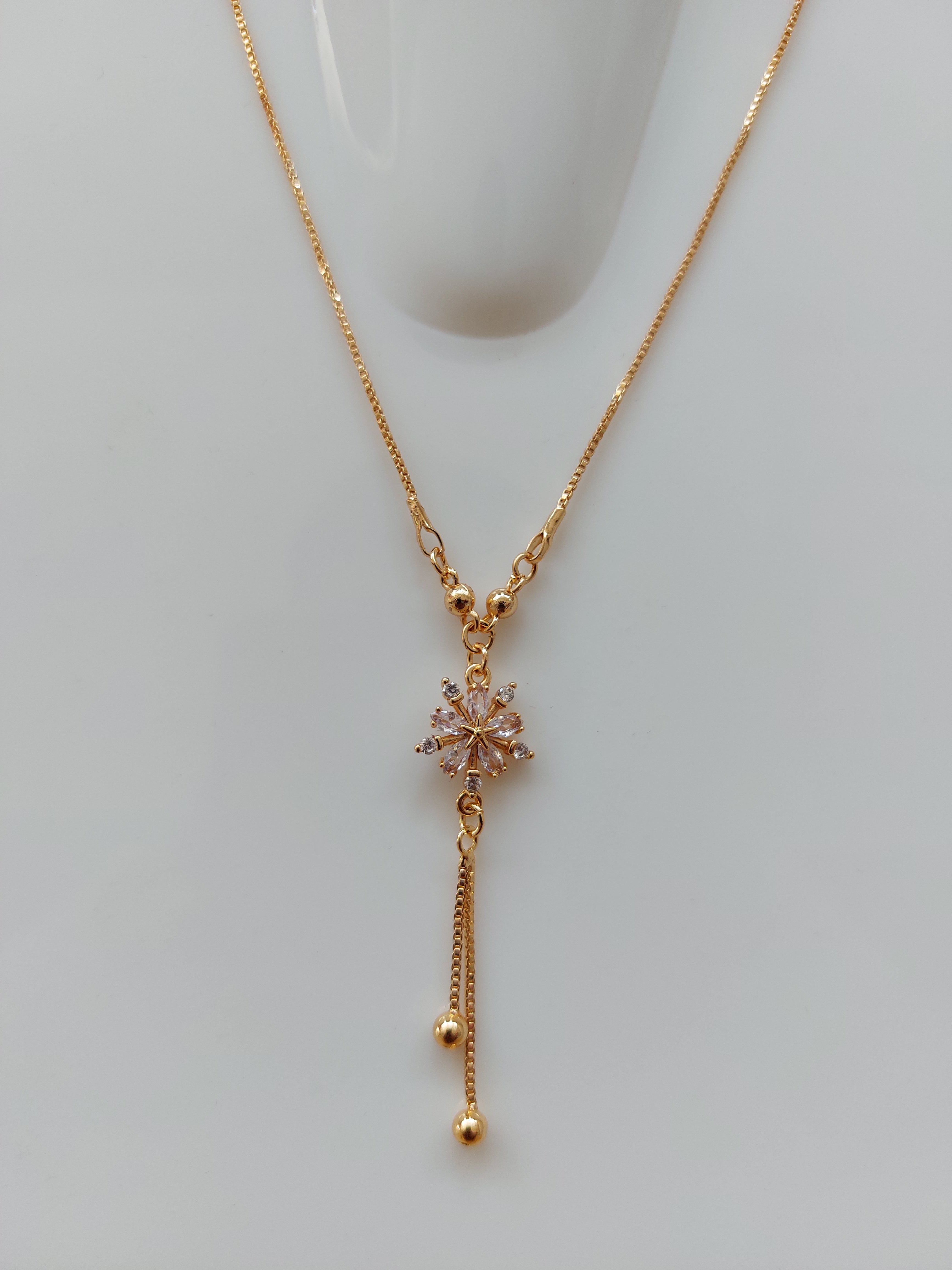 A delicate gold Y-necklace with a central snowflake charm adorned with small clear crystals, resting on a light gray surface.